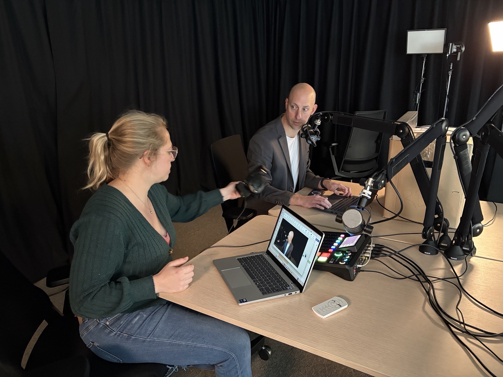 De ECP Studio: overzicht van de tafel met RØDE-microfoons, laptops, een audiomixer en de camera- en lichtopstelling tegen een zwarte studioachtergrond.